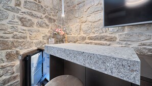 A stone wall interior with a built-in kitchen counter, a television mounted above, and a small flower arrangement on the counter.