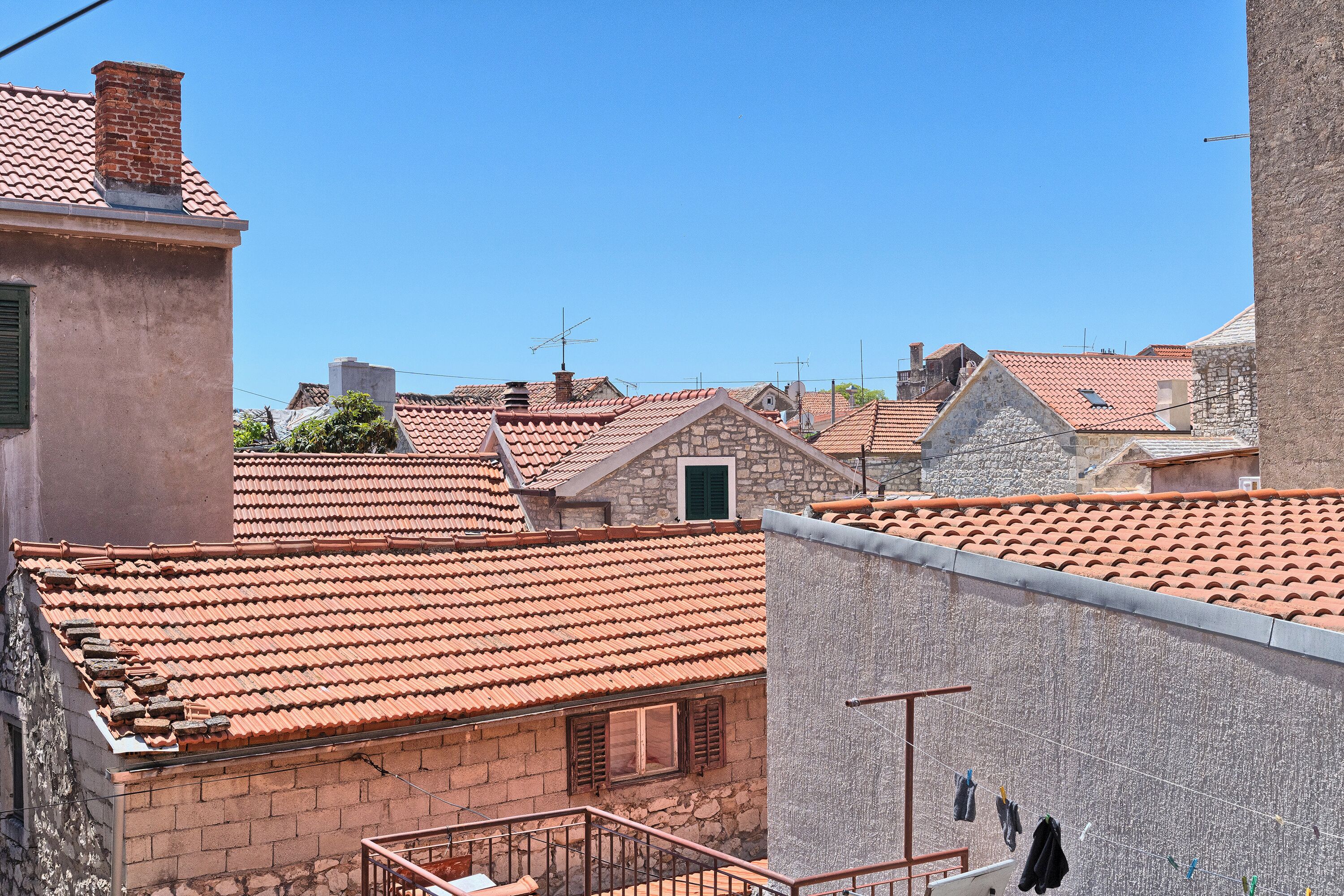 A residential area with terracotta-tiled roofs, stone buildings, and a visible laundry line.