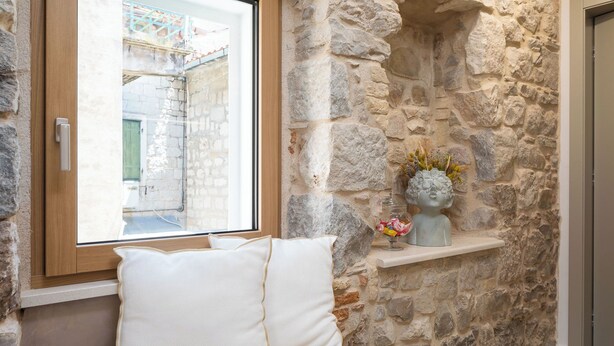A stone wall with a window, a cushioned bench, and a small shelf with a decorative item.