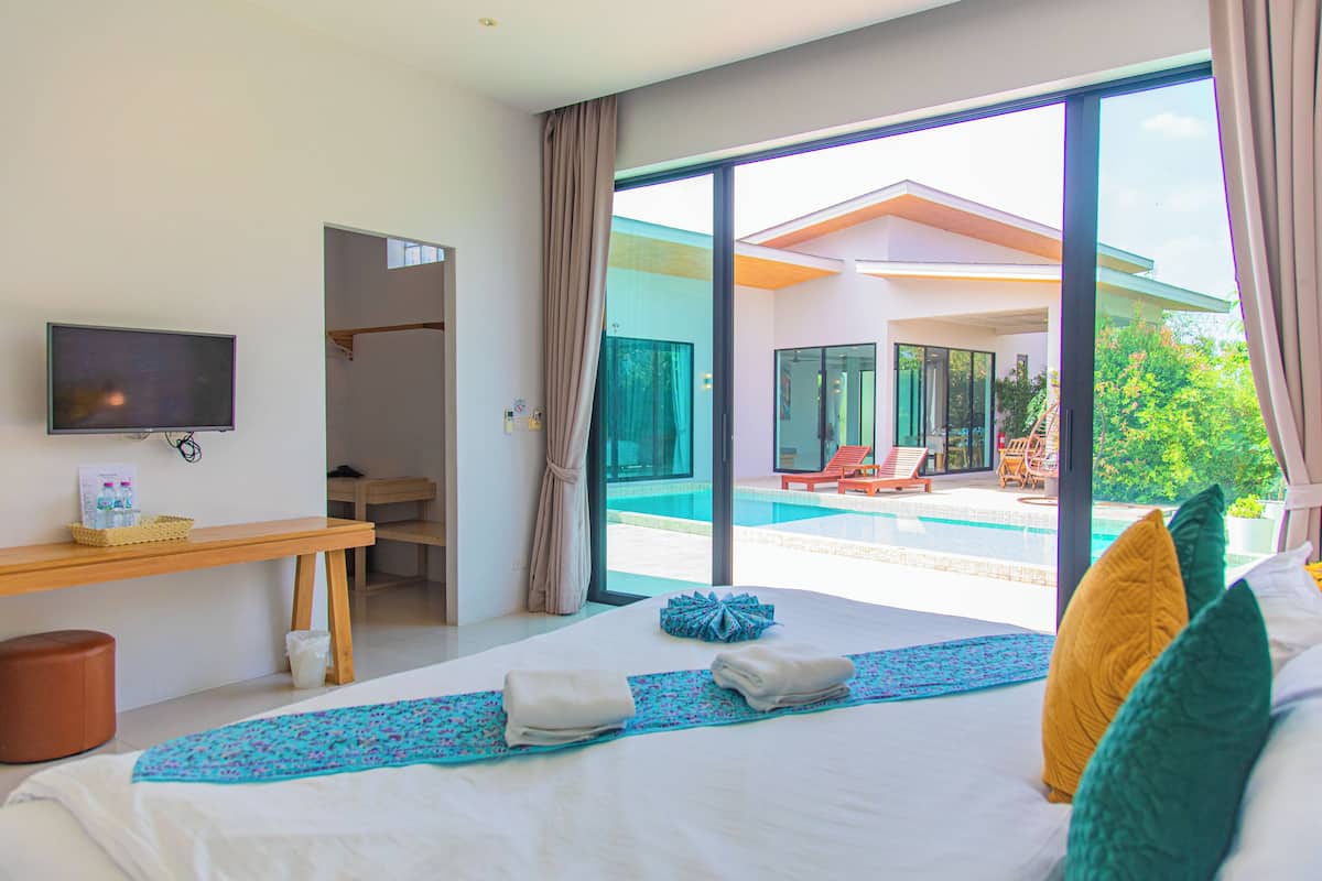 A hotel room with a bed, a TV, a desk, and a view of a swimming pool.
