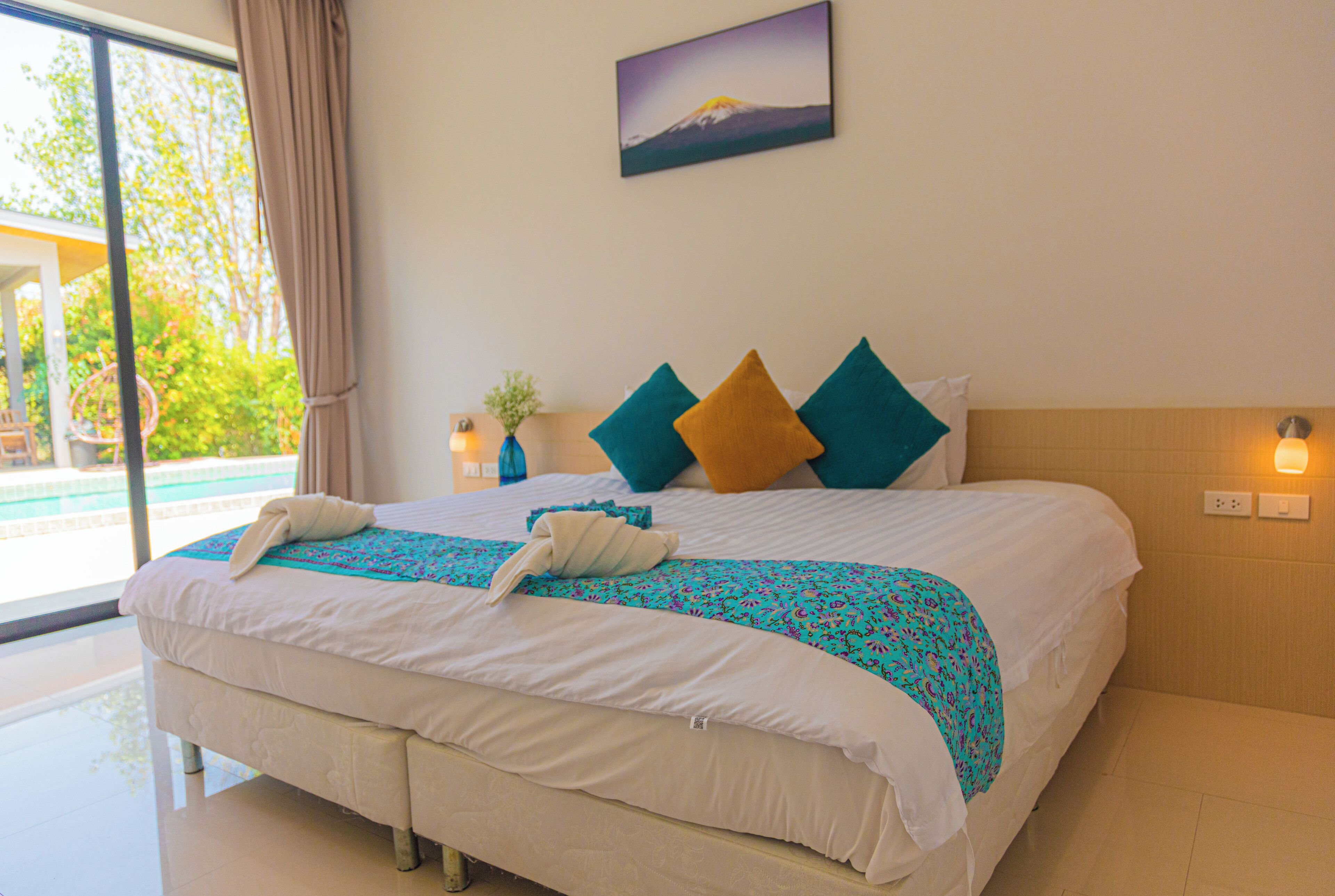 Un lit bien fait, recouvert d’une couvre-lit à motifs bleus et blancs, avec deux oreillers turquoise et moutarde, et une couverture blanche.
