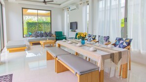 A modern dining area with a long table, benches, and a television. - Alhambra Pool Villas & Pool Access Rooms (Rawai)