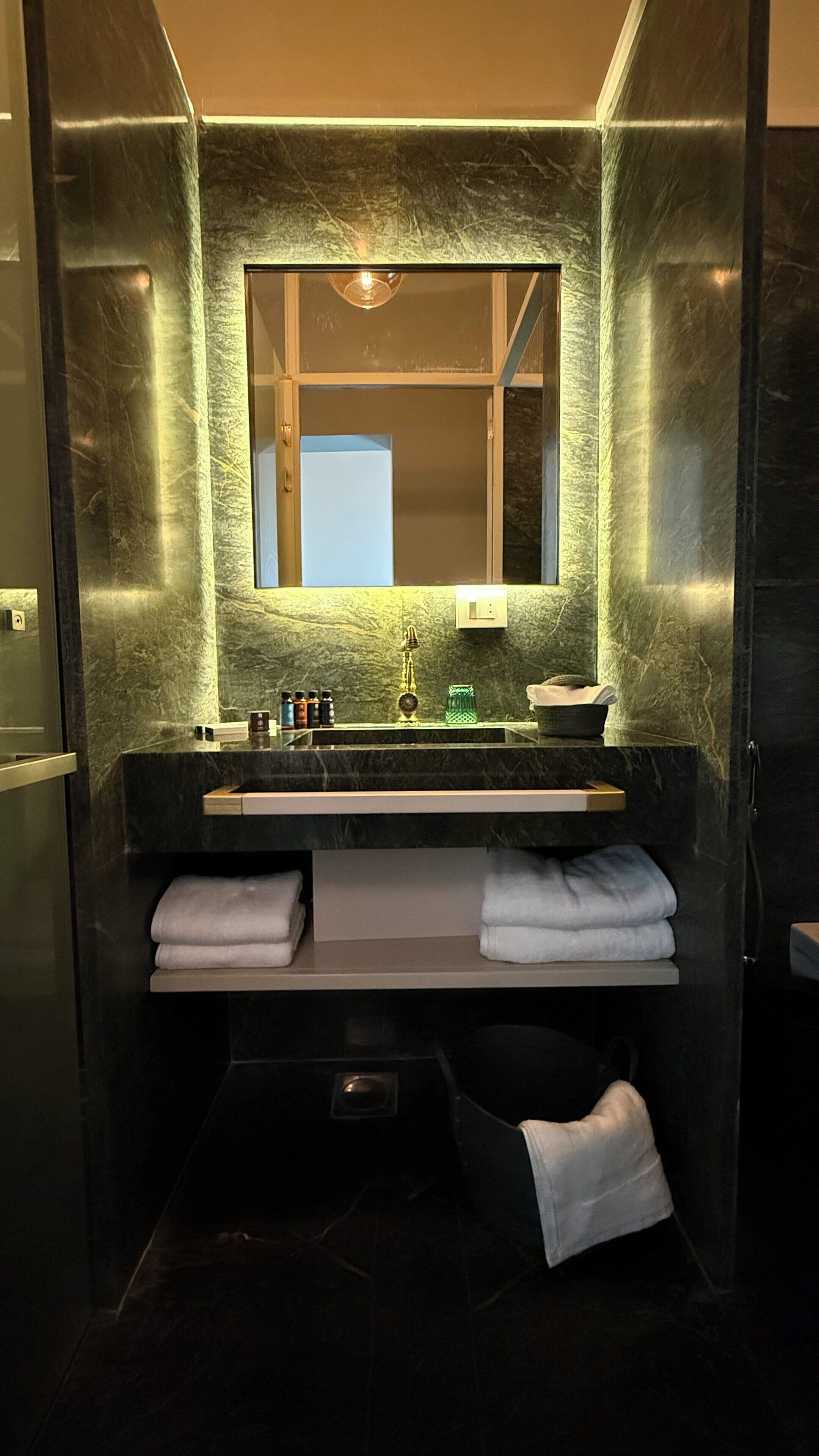 A modern bathroom with a marble sink, a large mirror, and two white towels on a shelf.
