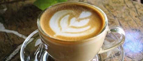 Una taza de café con arte de latte sobre un platillo de vidrio transparente sobre superficie texturizada.