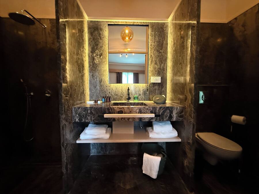 Un baño moderno con tocador de mármol, un espejo grande, una ducha y un inodoro.