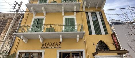 A yellow building with a sign reading "MAMAZ KITCHEN" and a balcony with a fan.