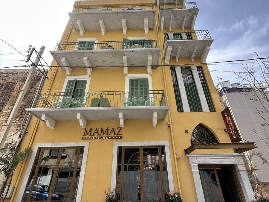 A yellow building with a sign reading "MAMAZ KITCHEN" and a balcony with a fan.