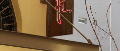 A building with a yellow facade, a wooden sign with red neon letters spelling "Lost," and a window with a decorative metal grill.