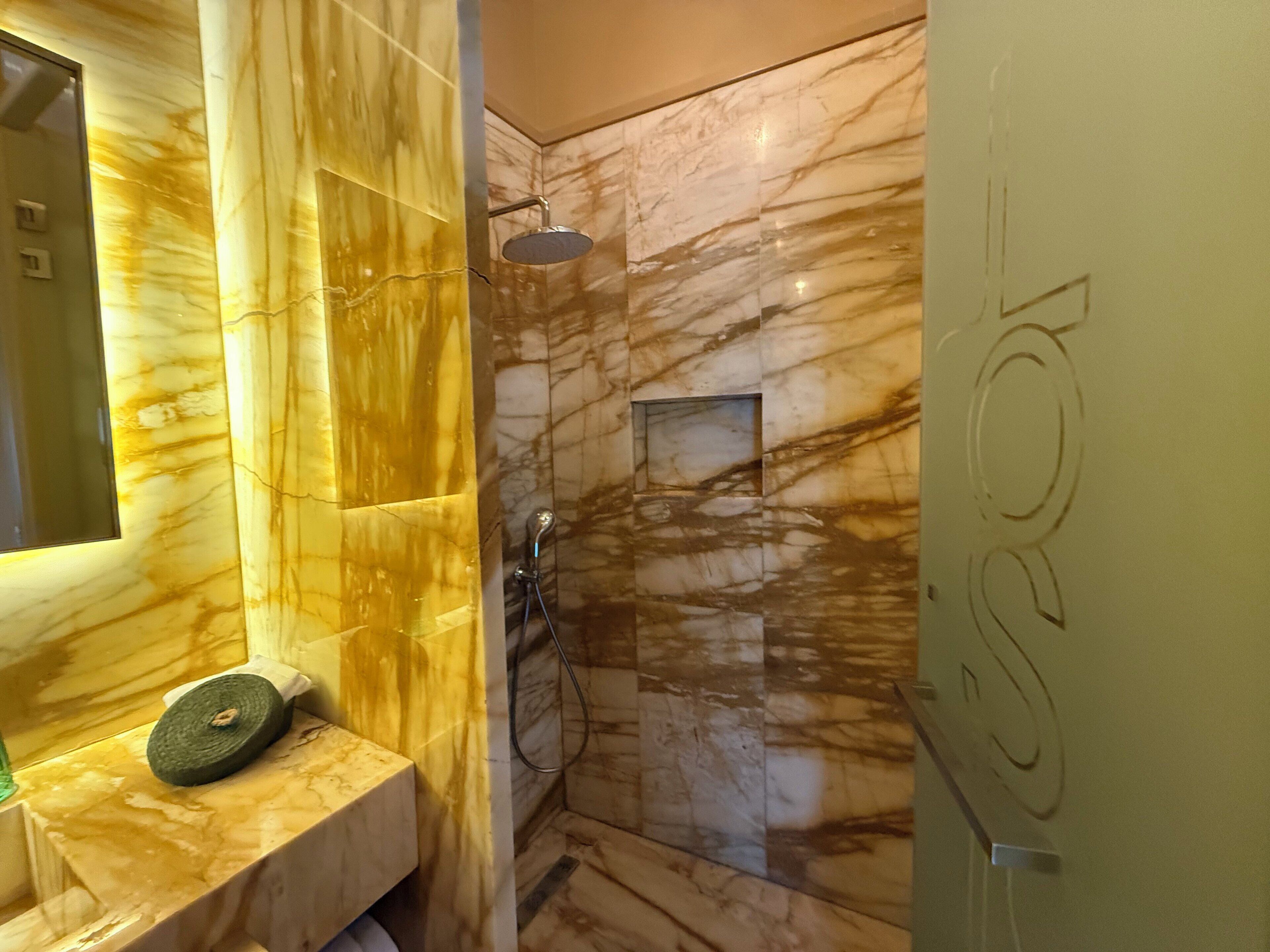 Une salle de bain avec un meuble-lavabo en marbre, une douche équipée d’un pommeau de douche à main et un miroir.
