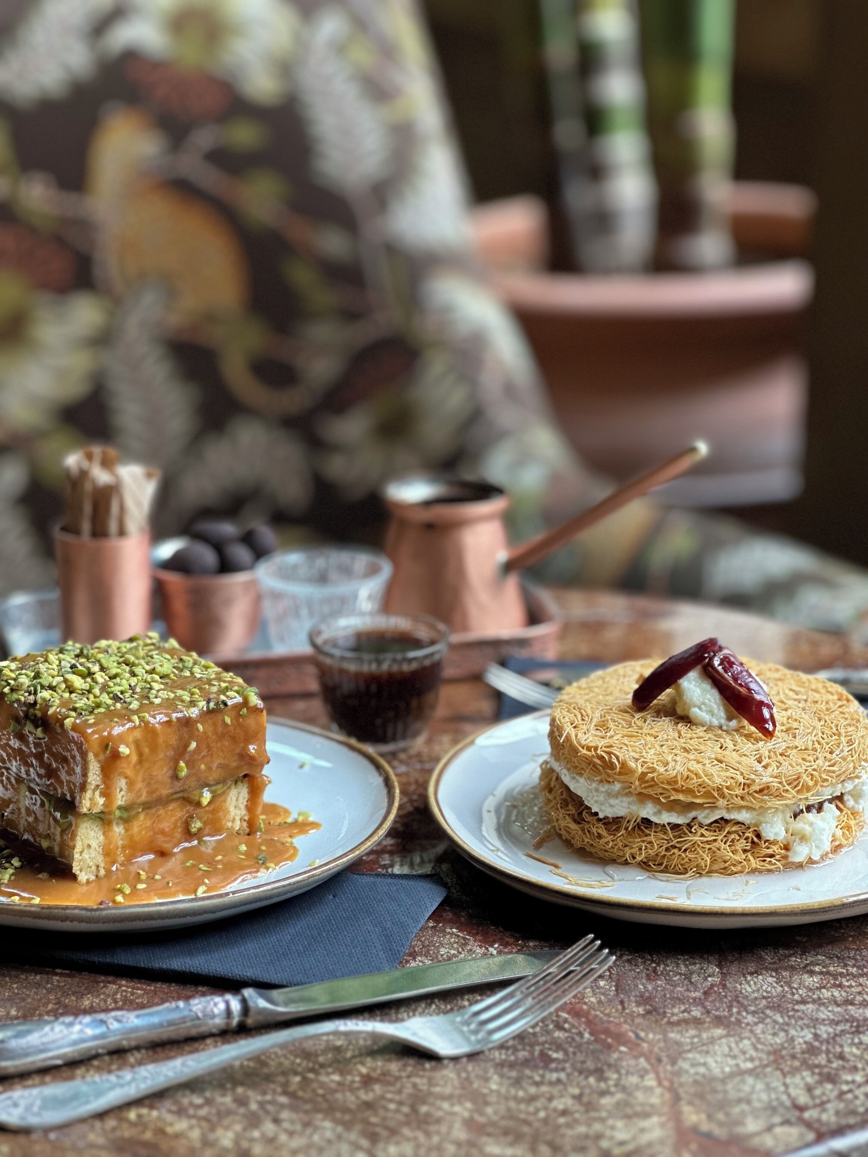 A table with two plates of dessert, a cup of coffee, and a fork.