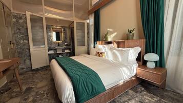 A hotel room with a large bed, a wooden nightstand, a mirror, a bathroom with a marble wall, and a green curtain.