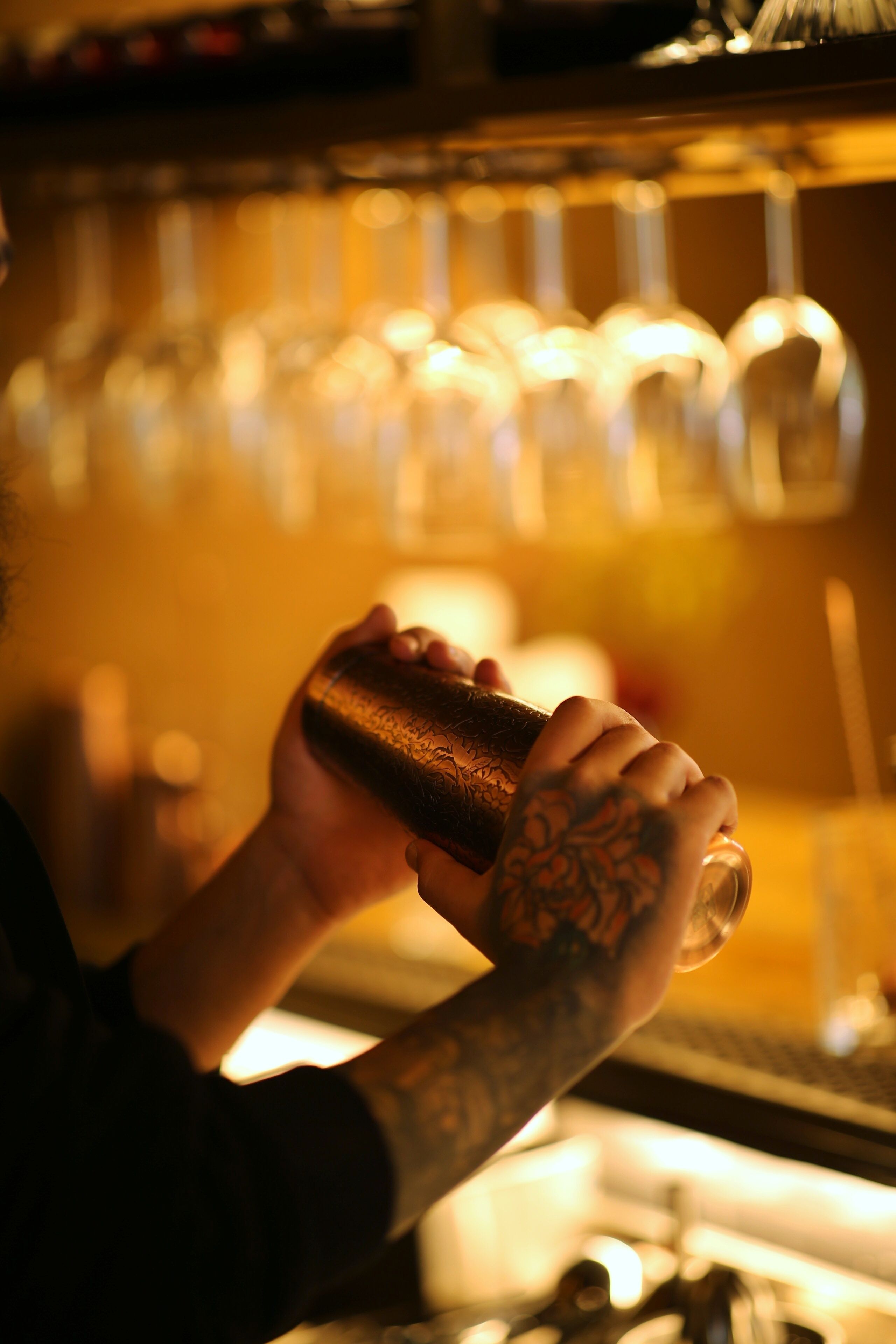 A person holding a bottle, with a background of hanging glasses.