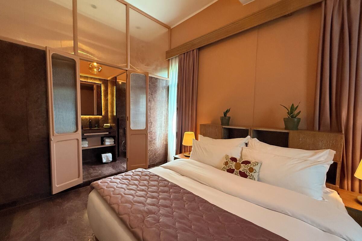 Une chambre d’hôtel avec un grand lit, un dressing, une coiffeuse avec un miroir et une plante en pot sur la table de chevet.