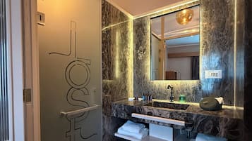 Un baño moderno con tocador de mármol, un espejo grande y una puerta de vidrio con una lámpara colgante.