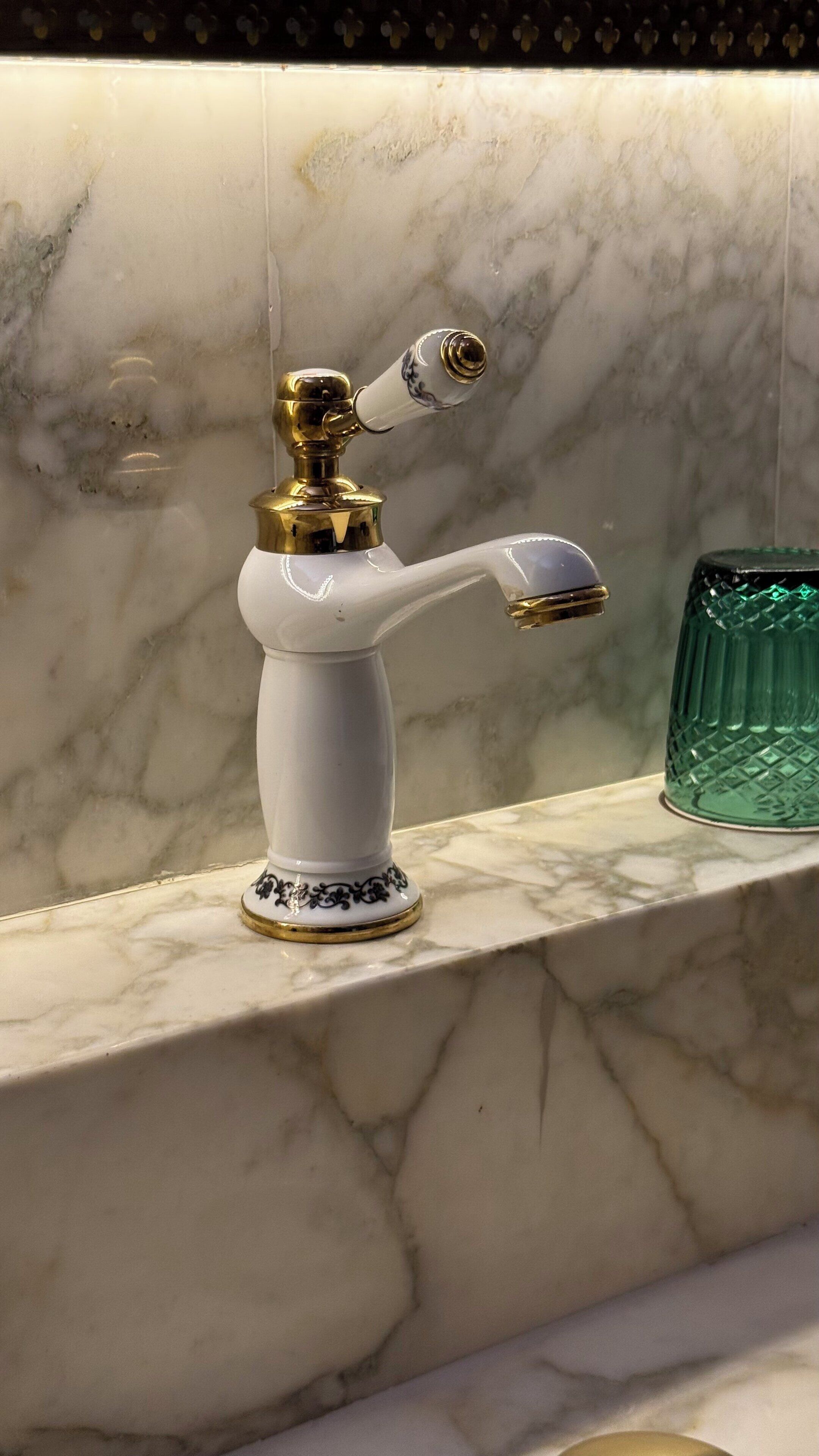 A bathroom with a marble sink and a gold and white faucet.