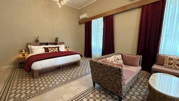 A bedroom with a bed, a sofa, a chair, a patterned floor, and a chandelier.
