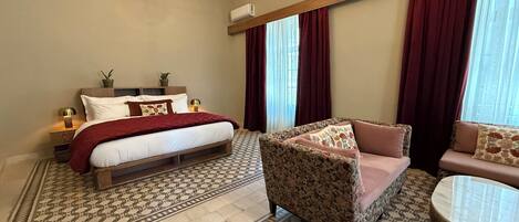 Un dormitorio con cama, sofá, sillón, suelo estampado y candelabro.