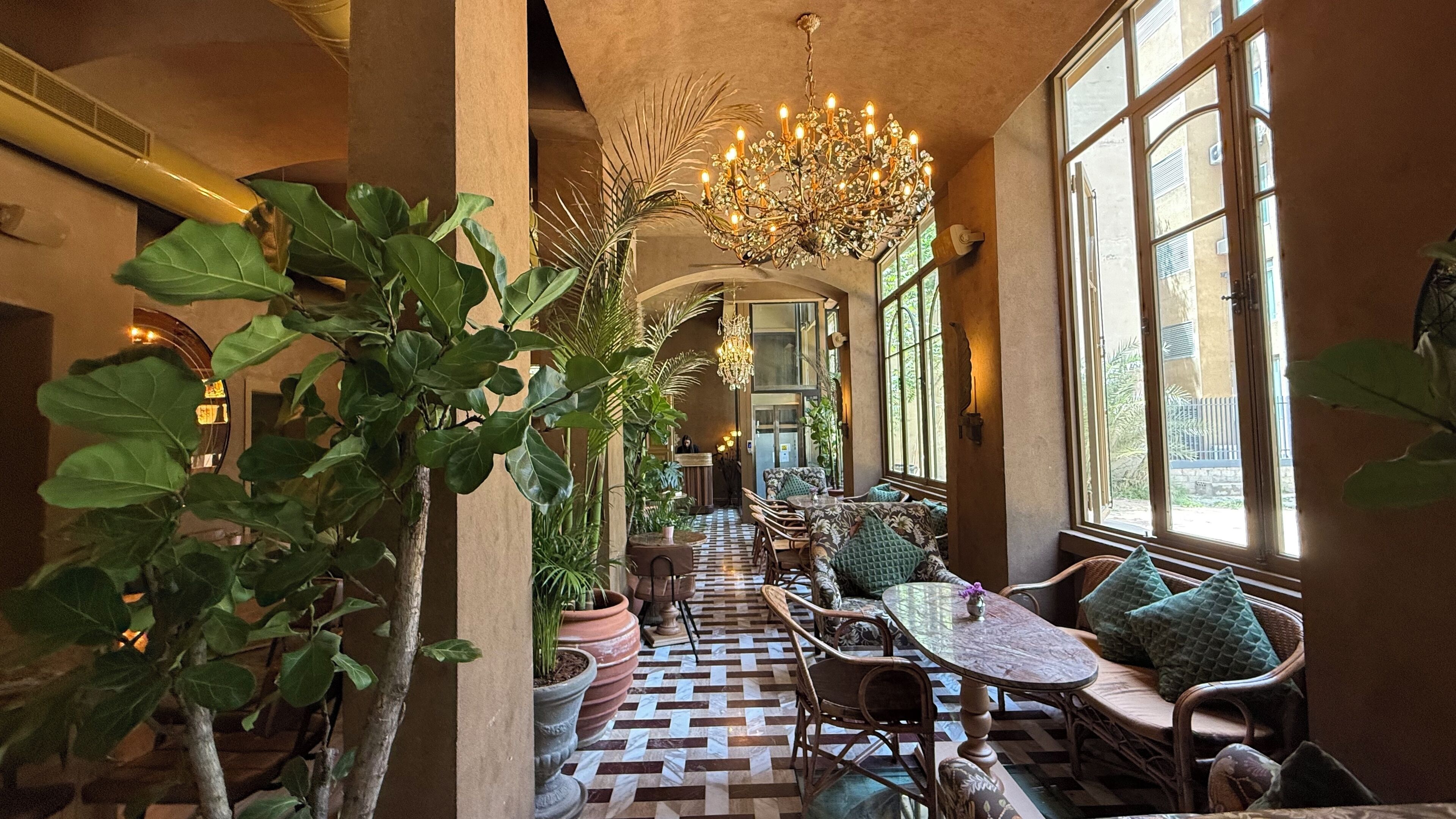 A corridor with a checkered floor, a chandelier, and seating areas with cushions.