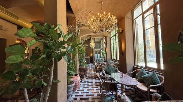 A corridor with a checkered floor, a chandelier, and seating areas with cushions.