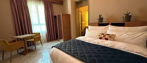 Habitación de hotel con cama, escritorio, silla, armario y dos plantas en macetas.