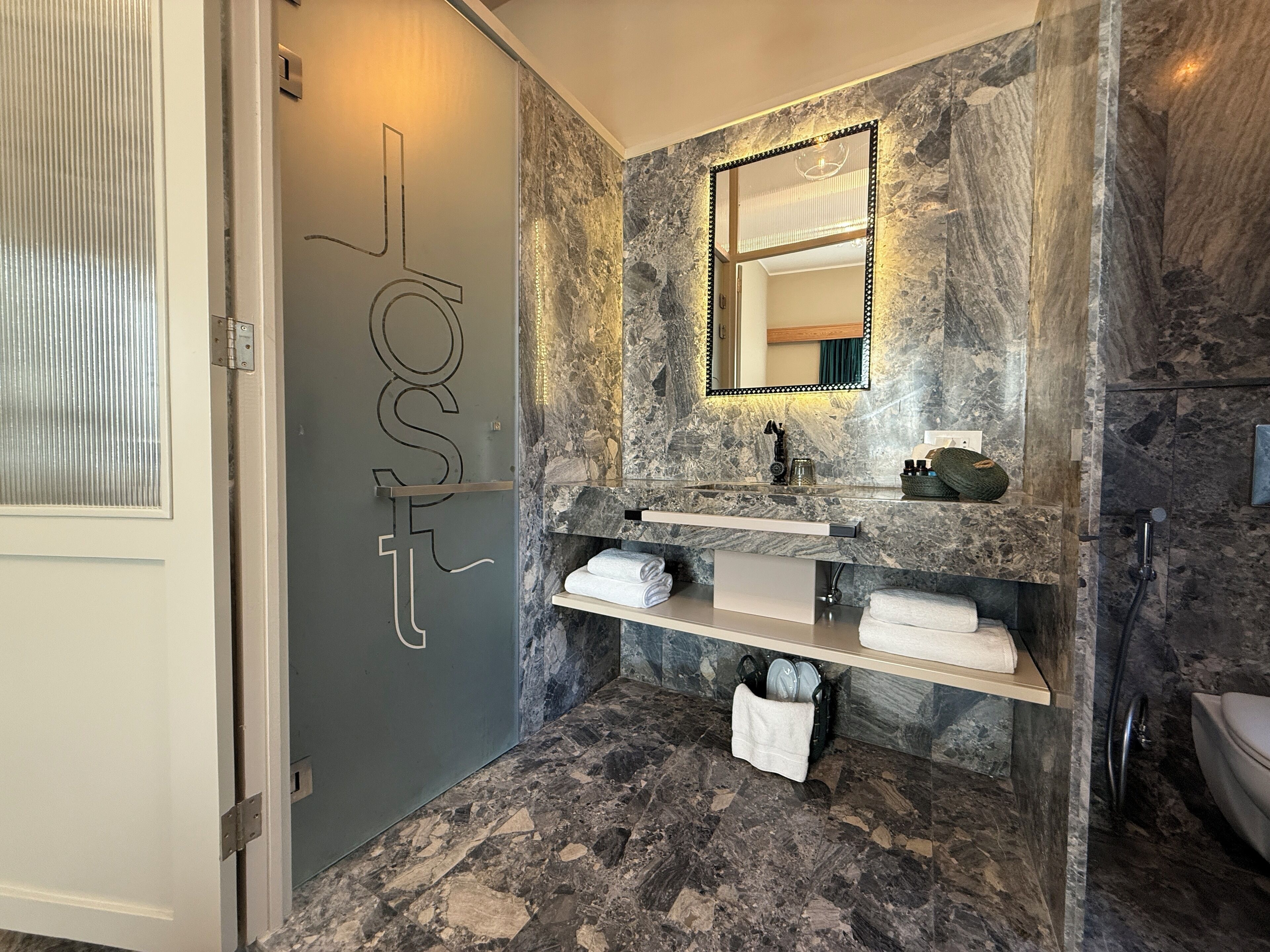 A bathroom with a marble wall, a sink with a mirror, and a shower area.
