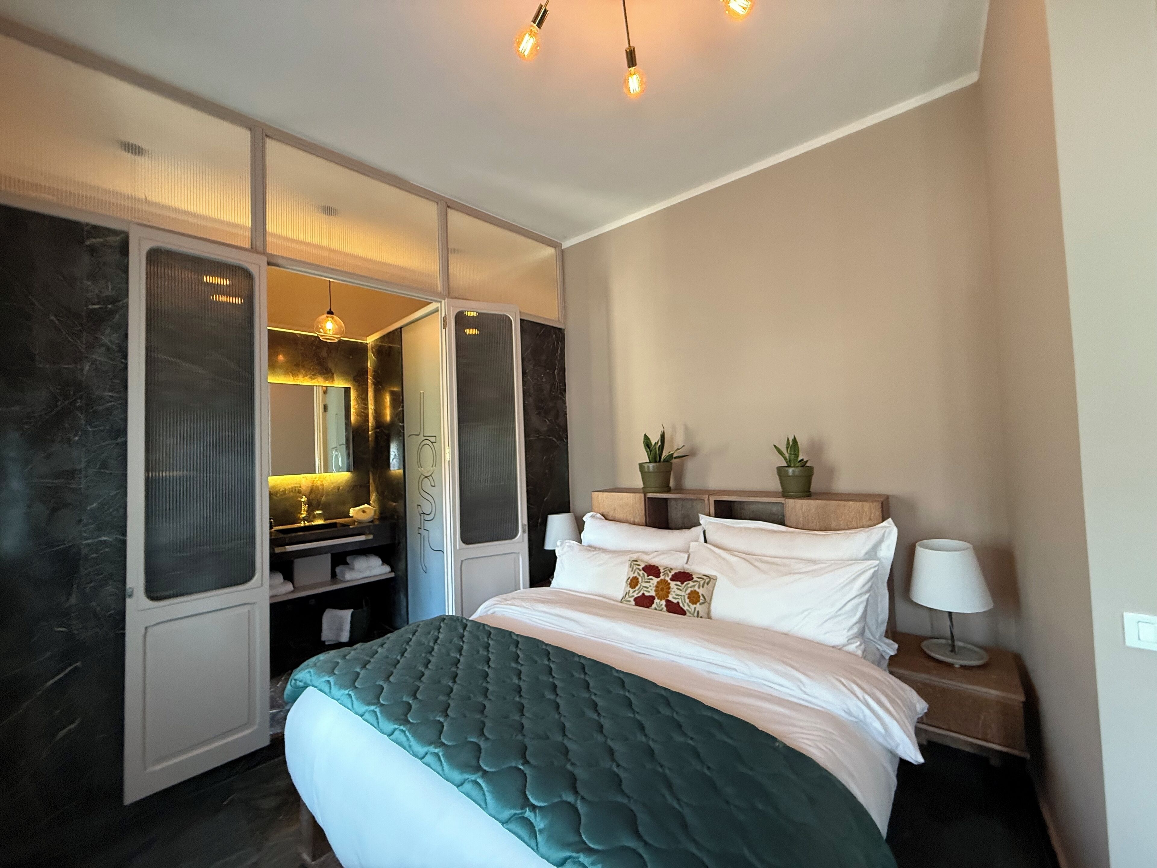 Une chambre à coucher moderne avec un grand lit, un dressing, une coiffeuse avec un miroir et deux plantes en pot sur la table de chevet.
