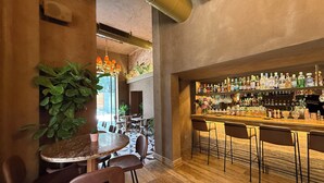 Un espace bar doté d’un comptoir en bois, de plusieurs options d’assises et d’une variété de bouteilles et de verres exposés sur des étagères.