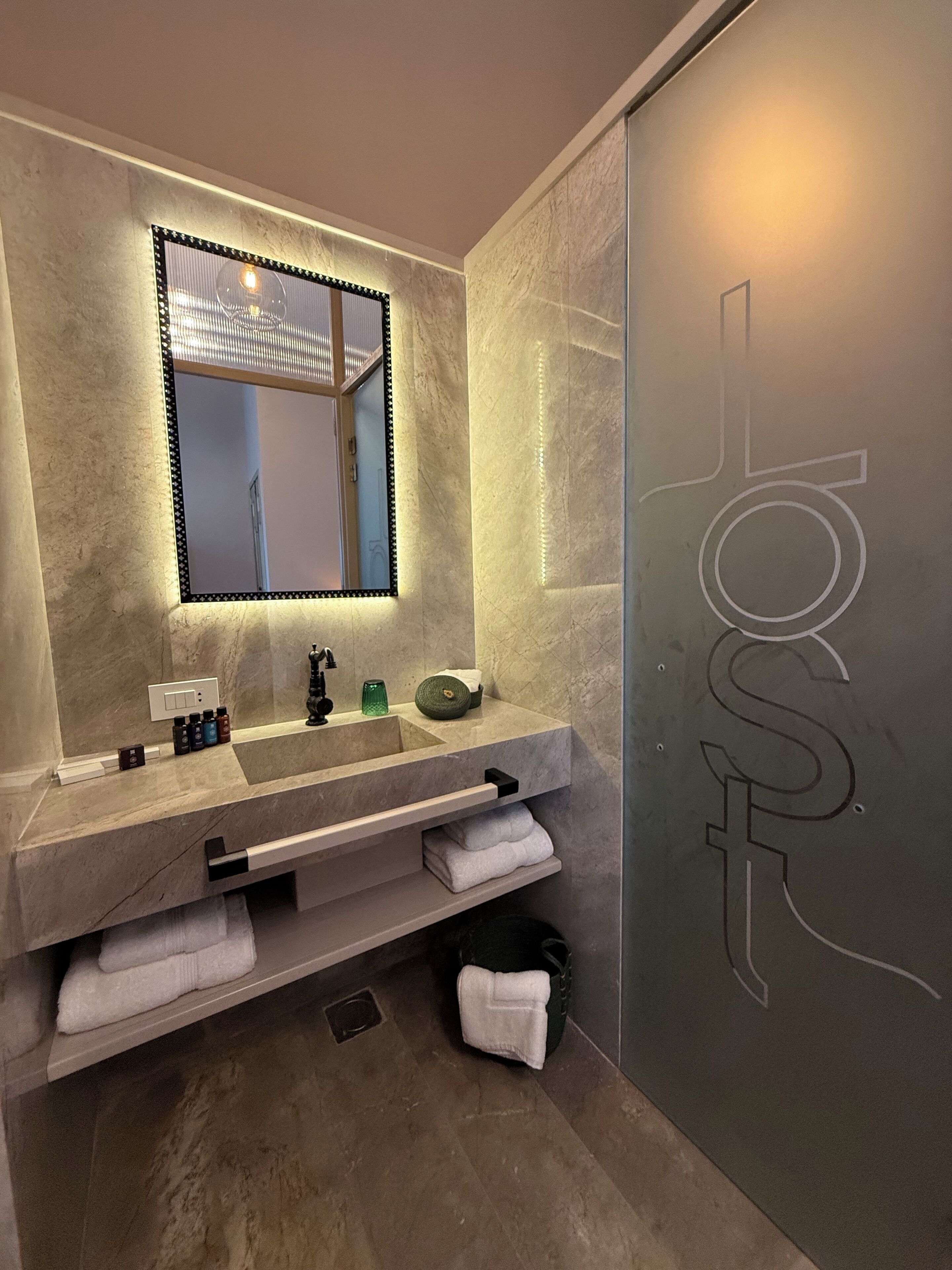 Un baño moderno con un espejo grande, un lavabo con varias botellas y un perchero para toallas.