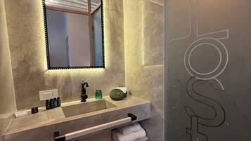 Un baño moderno con un espejo grande, un lavabo con varias botellas y un perchero para toallas.