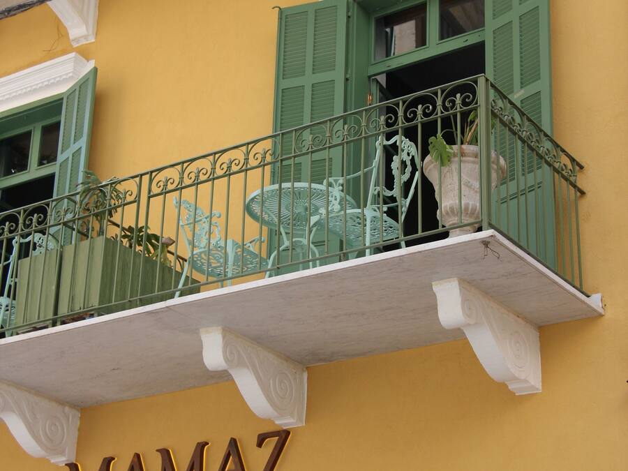 Un edificio con fachada amarilla, contraventanas verdes y un balcón con barandillas de metal. Se ve el letrero "MAMAZ KITCHEN".