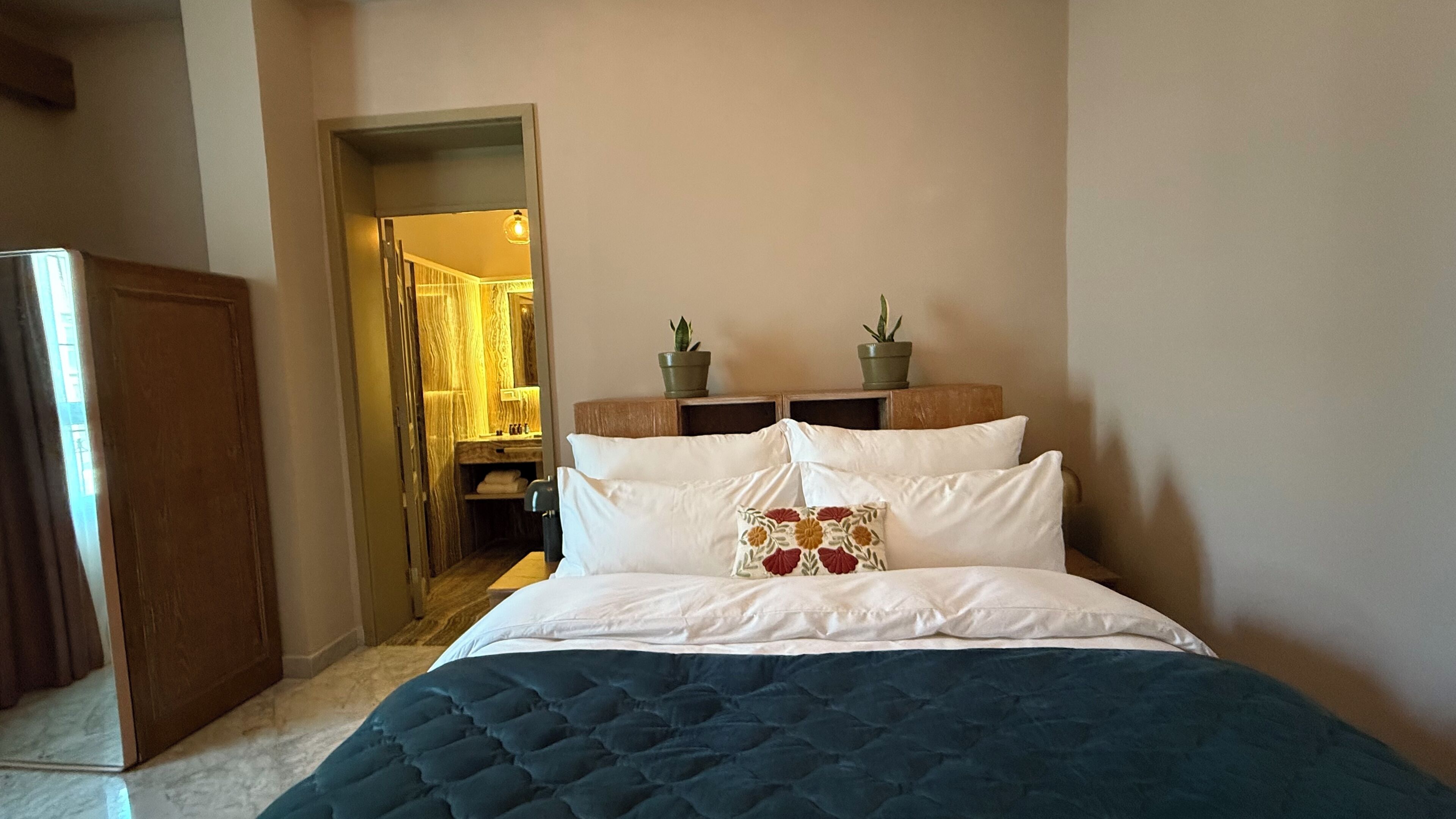A bedroom with a bed, a nightstand, a mirror, and a door leading to a bathroom.