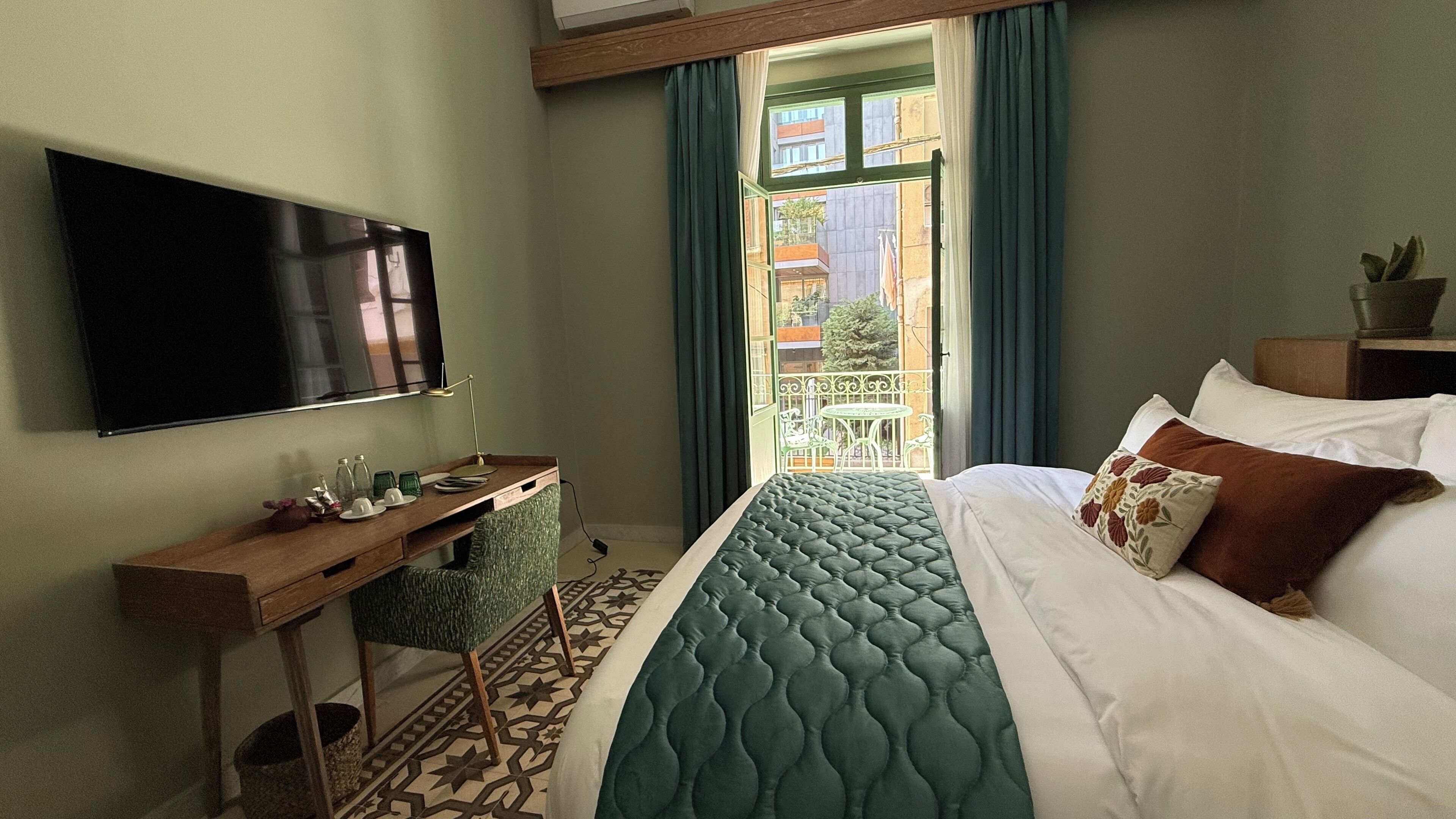 A hotel room with a bed, a desk, a TV, and a view of the outside balcony.