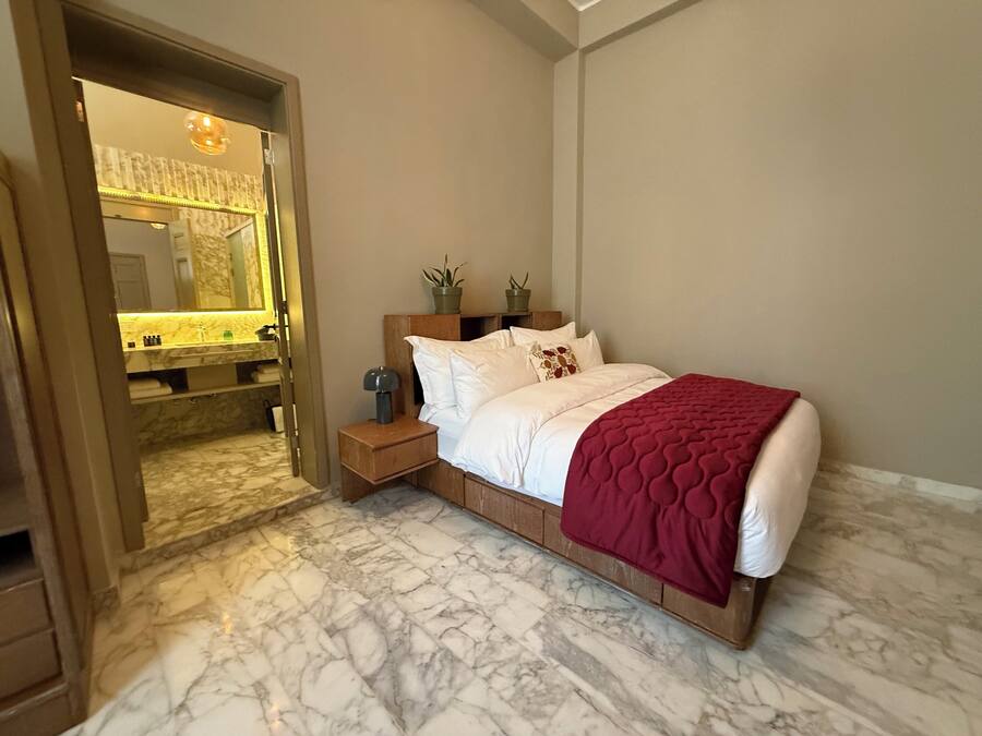 A bedroom with a marble floor, a wooden bed frame, a red blanket, and a nightstand with a lamp.