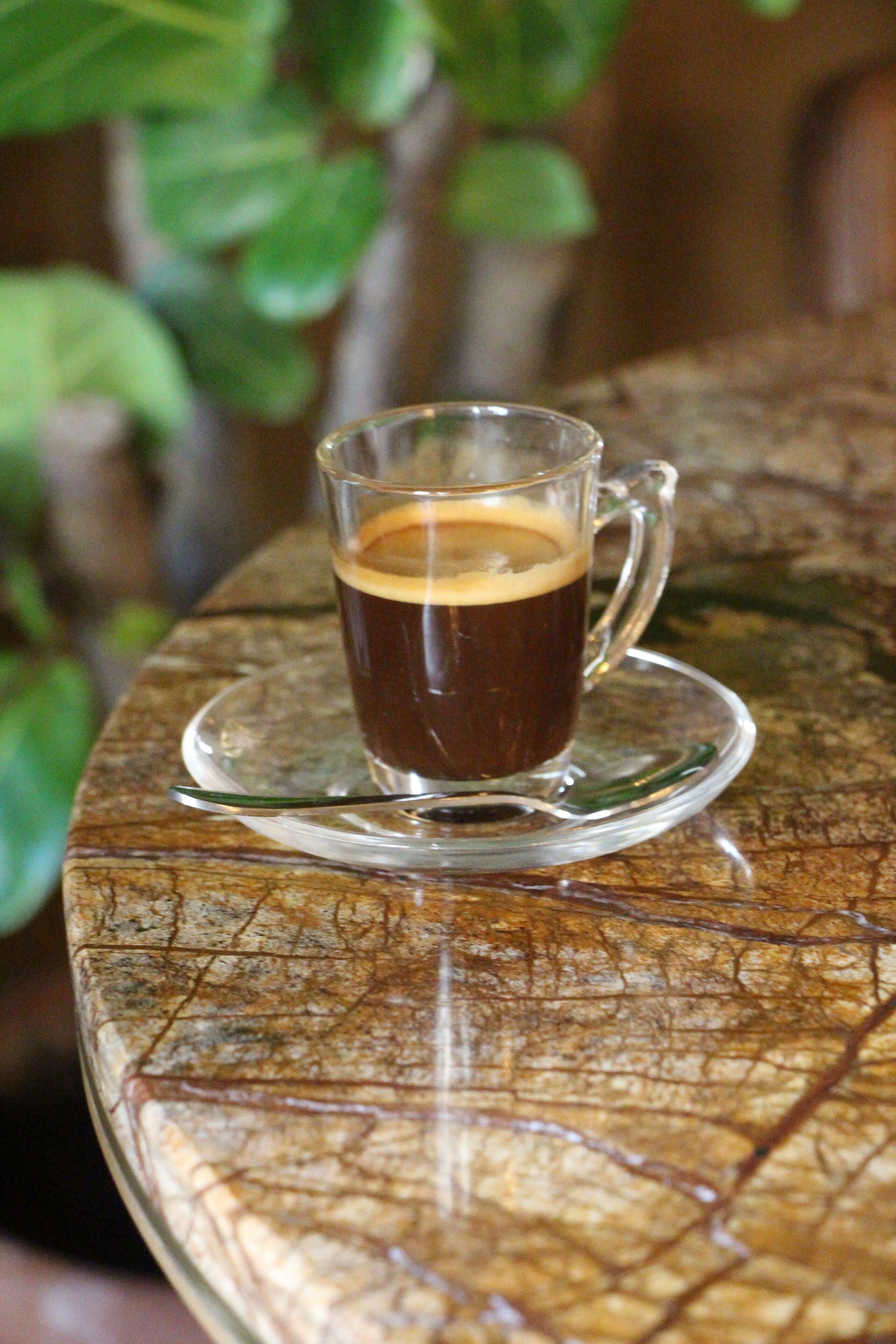 A glass cup of coffee on a textured table with a leaf pattern.