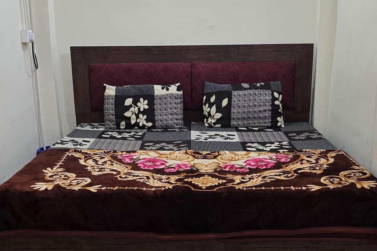 A bed with a dark headboard and multiple pillows, a patterned bedspread, and a white wall with a ceiling light fixture.