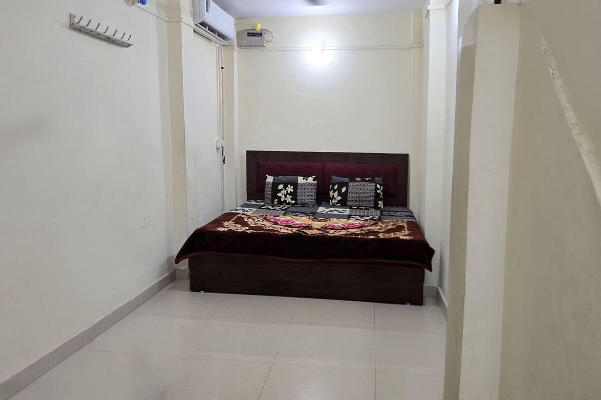 A narrow, well-lit room with a bed centered, featuring a dark headboard and floral-patterned bedding.