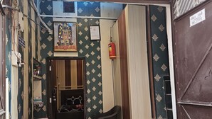 A hotel entrance with a signboard, a framed religious picture, a fire extinguisher, and a plastic chair outside. - Ramlala Paying Guest House (Ayodhya)