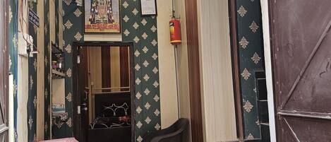 A hotel entrance with a signboard, a framed religious picture, a fire extinguisher, and a plastic chair outside.