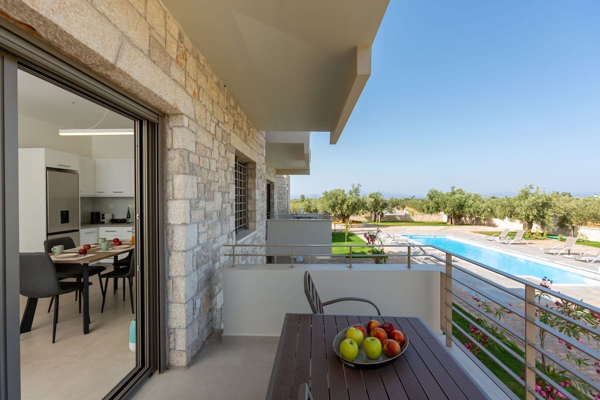 Ein Balkon mit Esstisch, Obstschale und Blick auf Pool und Grünflächen.