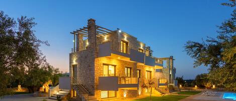 A modern two-story house with a stone facade, a swimming pool, and a well-lit outdoor area.
