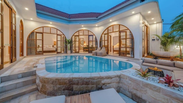 A modern pool area with a hot tub, stone steps, and a seating area with cushions.