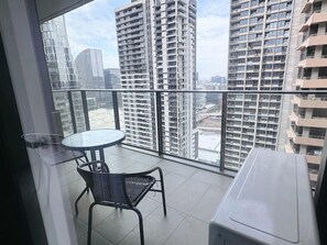 A balcony with a table and chairs, overlooking a cityscape with high-rise buildings.