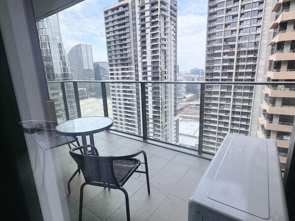 A balcony with a table and chairs, overlooking a cityscape with high-rise buildings.
