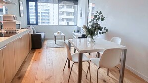 Ett modernt kök med matplats, trägolv och stora fönster som erbjuder utsikt över stadsbilden.