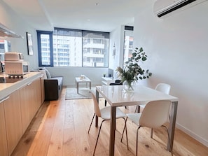 A modern kitchen with a dining area, wooden flooring, and large windows offering a view of the cityscape.