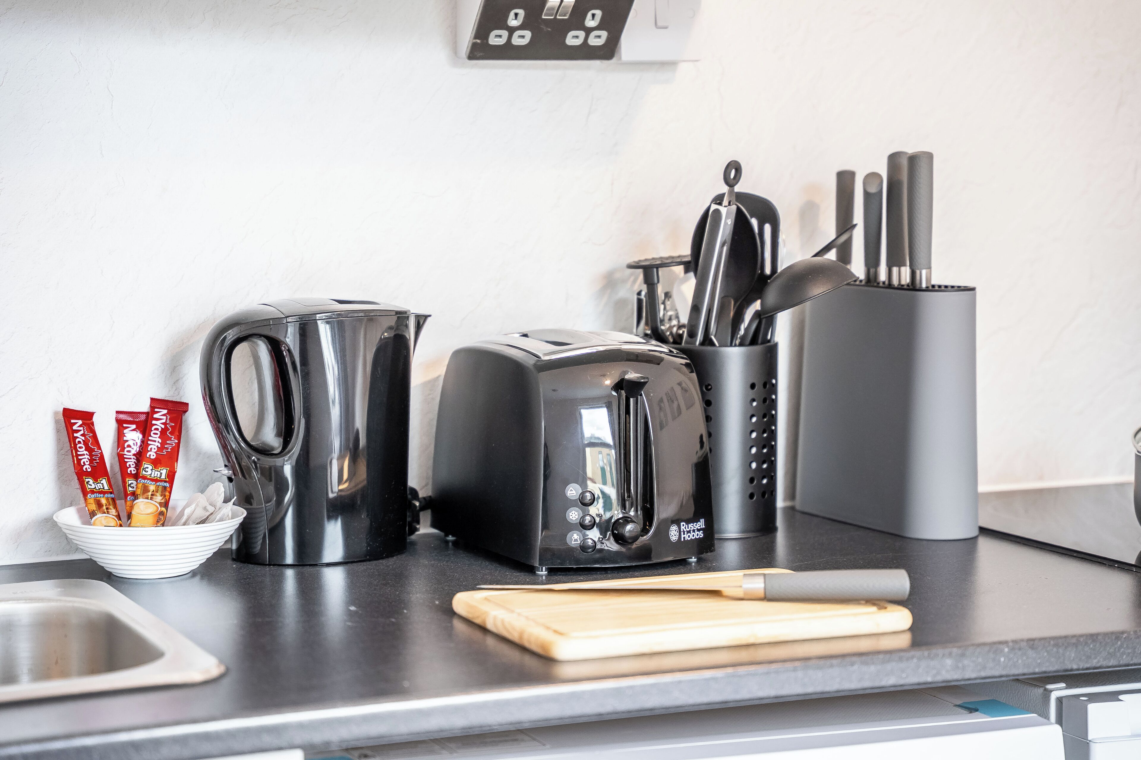 Eine Küchenarbeitsplatte mit Wasserkocher, Toaster, Kaffeekapseln, einem Messerblock und einem Schneidebrett.
