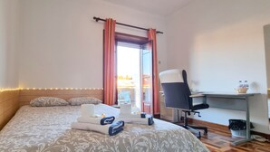 A hotel room with a bed, a desk, and a chair. There is a window with curtains, a view of the outside, and a small balcony. - CQ2 | Bedroom w/ Balcony | 3 min walk to HUC - Medicine - Pharmacy | Polo III (Coimbra)