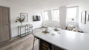 A modern kitchen with a central island, a dining area with chairs, and a large window providing natural light. - Stylish 2BR Apartment Near Preston City Centre (Preston)