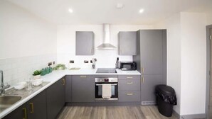 A modern kitchen with grey cabinets, a stainless steel sink, and a built-in oven. - Stylish 2BR Apartment Near Preston City Centre (Preston)