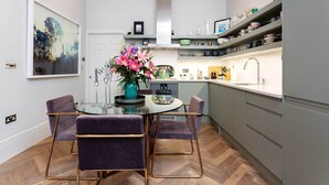 A modern kitchen with a dining area, featuring a glass table, purple chairs, and a teal vase with flowers. - Gateway to Notting Hill, by Veeve (London)